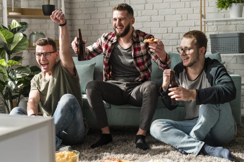 front-view-cheerful-male-friends-having-pizza-with-beer-watching-sports-tv